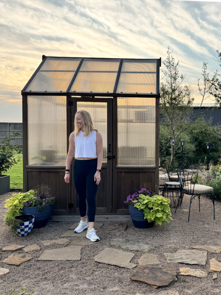 Julia standing in front of a greenhouse at sunrise with flower beds filling the frame